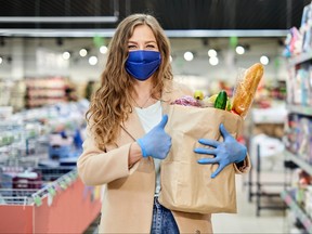Woman in a medical mask holds a paper bag with products and sign thumb up. Shopping during the covid-19 pandemic.