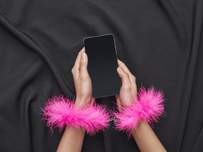 She is in your control. Female hands in pink furry handcuffs holding smartphone on a black silk fabric
