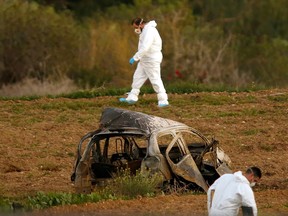 Forensic experts walk in a field after a bomb blew up a car (foreground) and killed investigative journalist Daphne Caruana Galizia in Bidnija, Malta, October 16, 2017.