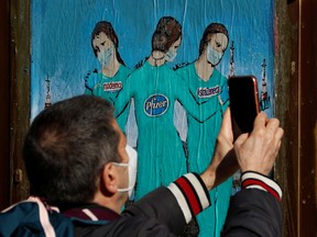 A man records a video of a painting representing Moderna, Pfizer and AstraZeneca vaccines in Barcelona, Spain, January 27, 2021.