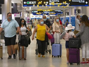 Travellers wearing protective face masks walking through Concourse D at the Miami International Airport on Sunday, Nov. 22, 2020, in Miami, Fla.