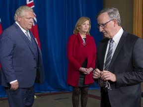 Dr. David Williams, Ontario's chief medical officer of health, left, turns from the microphone as Ontario Premier Doug Ford and Health Minister Christine Elliott look on in Toronto, Nov, 13, 2020.