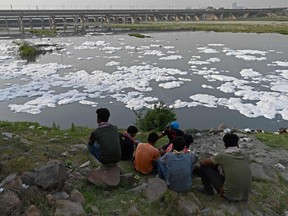 People sit on the banks of the river Yamuna — half covered with foam caused by pollution — on the eve of World Water Day in New Delhi on March 21, 2021.