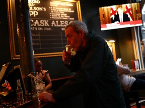 A man with a drink as Britain's Prime Minister Boris Johnson, is seen on a television screen in a pub in London.