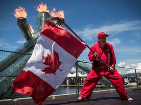 Ricky Johnson waves a Canadian flag on a hockey stick as the Olympic cauldron burns while attending Canada Day celebrations in Vancouver, on Monday July 1, 2019.