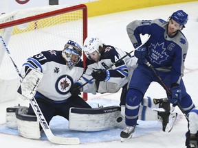 Winnipeg Jets goaltender Connor Hellebuyck makes a pad save as Maple Leafs' John Tavares (and Jets defenceman Josh Morrissey battle for the loose puck during the third period in Toronto on Tuesday, March 9, 2021.