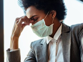 Black businesswoman with protective face mask holding her head in pain.