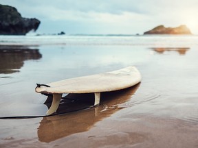 A board for surfing is pictured on a deserted ocean beach.