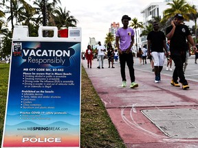 A sign asking vacationers to follow Covid-19 safety protocols is seen as people walk on Ocean Drive in Miami Beach, on March 22, 2021.