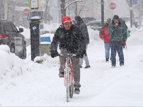 A cyclist and pedestrians navigate a snow-covered sidewalk on Durham Street in Sudbury, Ont. on Wednesday Feb. 24, 2021.