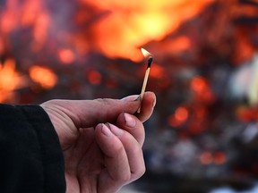 An image of a man's hand holding an open flame with a large fire in the background.