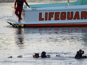 FILE - In this April 9, 2015, file photo, divers emerge from the water as debris believed to be from a car floats to the surface where a car went off a pier and into the water in Los Angeles' San Pedro harbor district.