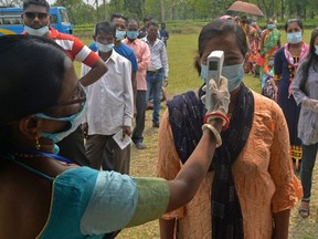 An official records body temperature of voters queueing up at a polling station to cast their ballot during the 5th phase of West Bengal's state legislative assembly elections in Mohorgon Tea estate on the outskirts of Siliguri on April 17, 2021.