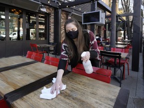 Rachel Nelson, shift manager/server at Hudsons Canada's Pub, sanitizes the sidewalk patio tables outside the establishment in Edmonton's Old Strathcona district on Friday April 9, 2021, after the provincial government imposed new COVID-19 health restrictions in Alberta, ordering all restaurants to close indoor dining.