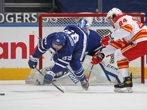 Maple Leafs forward Nick Robertson (left) clears the puck against the Calgary Flames on Tuesday night at Scotiabank Arena. Robertson was placed on the list of NHL players who are unavailable because of COVID protocol.