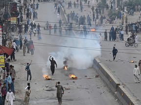 Supporters of Tehreek-e-Labbaik Pakistan (TLP) party block a road as riot policemen fire teargas shell during a protest against the arrest of their leader as he was demanding the expulsion of the French ambassador over depictions of Prophet Muhammad, in Islamabad on April 13, 2021.