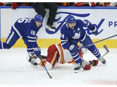Calgary Flames Andrew Mangiapane LW (88) is flattened to the ice by Toronto Maple Leafs Mitch Marner RW (16) and teammate Auston Matthews (34) during the first period in Toronto on Tuesday April 13, 2021. Jack Boland/Toronto Sun/Postmedia Network
