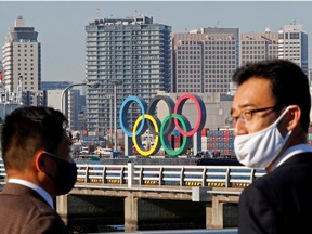 Men wearing face masks watch as giant Olympic rings, which were temporarily taken down in August for maintenance amid the coronavirus disease (COVID-19) outbreak, are transported for reinstallation at the waterfront area at Odaiba Marine Park in Tokyo, Japan December 1, 2020.