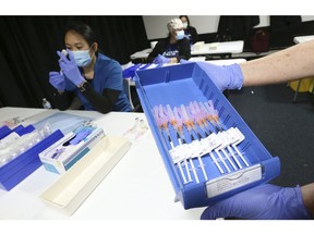 Helen Briggs, a pharmacist, holds up a tray of syringes as Lirie Palamind an RPN (background) loads up them up with Pfizer-BioNTech COVID-19 vaccine at the Humber River Hospital clinic held at Downsview Arena on April 21, 2021.