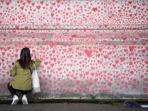 A woman writes a message on a heart painted on the National COVID Memorial Wall on the south side of the River Thames in London on May 28, 2021, in memory of those who lost their lives to COVID-19.