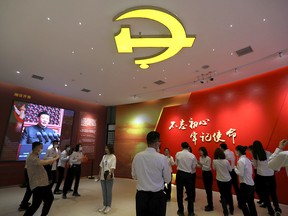 People stand under the Communist Party of China emblem near an image of Chinese President Xi Jinping at Xibaipo Memorial Hall during a government-organized tour in Xibaipo, China May 12, 2021.