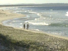 In this image made from a video, people walk along a beach in Tuncurry, Australia, Tuesday, May 18, 2021. A surfer was killed by a shark on Tuesday, police said.