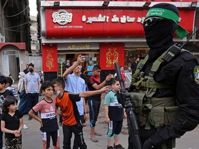 Palestinian boys look  at members of Al-Qassam brigades, the armed wing of Palestinian Hamas group, marching in Gaza City on May 22, 2021, in commemoration of Senior Hamas Commander Bassem Issa who was killed along others in Israeli airstrikes.