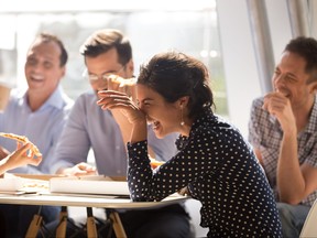 Indian woman laughing eating pizza with diverse coworkers in office