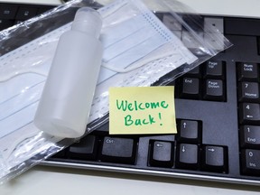 Welcome back note with hand sanitizer and mask on top of keyboard