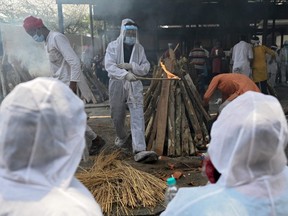 A family member (centre) wearing protective gear performs the last rites of a victim who died of COVID-19 at a crematorium in Ghazipur, India, Saturday, May 1, 2021.