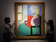 In this file photo taken on April 22, 2021 gallery workers display an artwork titled 'Femme assise pres d'une fenetre (Marie-Therese)' by Spanish painter Pablo Picasso during a photocall at Christies auction house in central London.