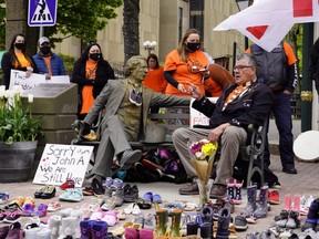 Elder Junior Peter Paul (sitting) points to a Sir John A. MacDonald statue next to 215 pairs of children's shoes placed in remembrance of the bodies discovered at the Kamloops Indian Residential School in British Columbia, during a ceremony in Charlottetown, P.E.I., Monday, May 31, 2021.