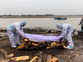 Men wearing protective suits place a white cloth over the body their relative, who died from the coronavirus disease (COVID-19), before his cremation on the banks of the river Ganges at Garhmukteshwar in the northern state of Uttar Pradesh, India, May 6, 2021.