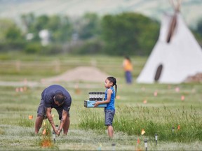 Members of the community place solar lights next to the flags which mark the spots where remains were discovered by ground penetrating radar at the site of the former Marieval Indian Residential School on the Cowessess First Nation, Sask., on June 26, 2021.
