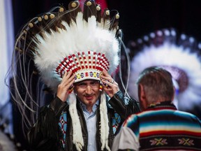 Prime Minister Justin Trudeau, left, adjusts his new headdress as Tom Heavenfire looks on during a ceremony while visiting the Tsuu T'ina First Nation near Calgary, Alta., Friday, March 4, 2016.