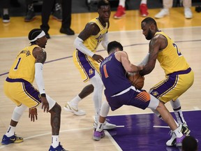 Devin Booker of the Phoenix Suns is tied up by LeBron James, right, of the Los Angeles Lakers as Dennis Schroder, centre, and Kentavious Caldwell-Pope, left, defend in a 113-100 Suns win during Game 6 of the Western Conference first round series at Staples Center on June 3, 2021 in Los Angeles, Calif.