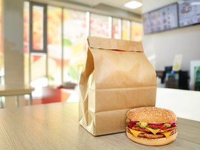 Cheeseburger and craft paper bag on wooden counter of cafe. Take out food concept. To go package mock-up.