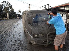 A resident cleans mud and ash from his car after Taal volcano began spewing ash over Tanauan town, Batangas province south of Manila on January 13, 2020.