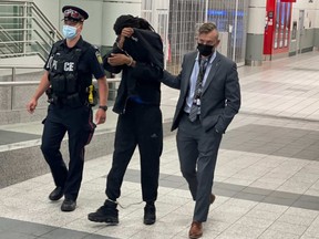 Malik Essue, 23, being escorted through Toronto Peearson Airport Thursday evening, back in Peel Region after being arrested in Fort McMurray in connection with the 2020 murder of Santiga Sharma.  He's charged with first-degree murder.