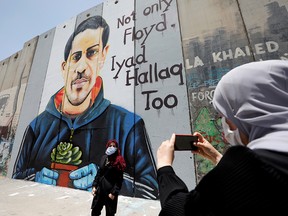 A Palestinian woman takes pictures of her friend posing in front of the Israeli barrier with a mural depicting Iyad al-Halaq in Bethlehem in the Israeli-occupied West Bank June 18, 2020.
