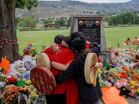 People from Mosakahiken Cree Nation hug in front of a makeshift memorial at the former Kamloops Indian Residential School to honour the 215 children whose remains have been discovered buried near the facility, in Kamloops, B.C., Friday, June 4, 2021.
