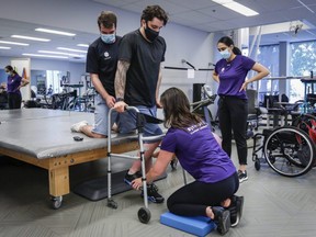 Humboldt Broncos bus crash survivor Ryan Straschnitzki, centre, is helped to stand in a walker by Eric Daigle, left, and Jill Mack, centre right,  while he attends a physiotherapy session in Calgary, Thursday, June 24, 2021.
