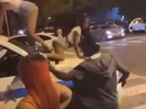 Onlookers watch on as two women twerk atop a moving police vehicle.