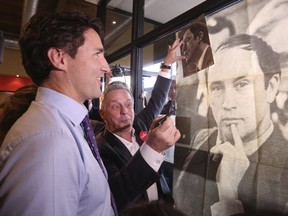 Prime Minister Justin Trudeau looks at a poster of his late father, former prime minister Pierre Trudeau, during a campaign stop at a coffee shop in Sainte-Therese, Que., on Oct. 15, 2015
