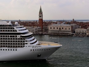 Tugboats escort the MSC Orchestra cruise ship across the basin past the Bell Tower and the Doge's palace as it leaves Venice on June 5, 2021.