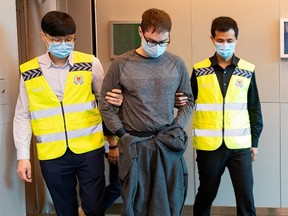 Police officers escort Canadian David James Roach in Singapore, March 2020, in this handout photo released to Reuters on July 8, 2021.