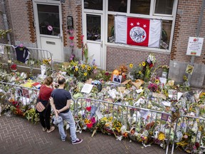 People stand by flowers laid in the Lange Leidsedwarsstraat in tribute to Dutch crime journalist Peter R de Vries, who was gunned down in broad daylight on July 6, 2021.