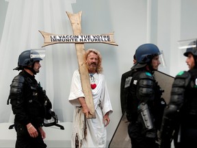 A protester dressed as Jesus Christ, holding a wooden cross reading "Vaccine kills your natural immunity," is surrounded by French Gendarmes on the Champs Elysees Avenue after clashes on the sidelines of a demonstration against France's restrictions to fight the COVID-19 outbreak, in Paris, July 24, 2021.