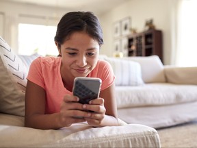 Teenage girl lying on the sofa at home in the living room using smartphone, close up, low angle, close up