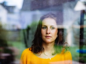 Young woman looks thoughtfully and sadly through the window into the garden with children's toys